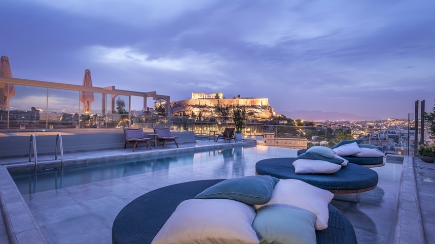 Pool with round sunbeds with cushions and view to the Acropolis at night