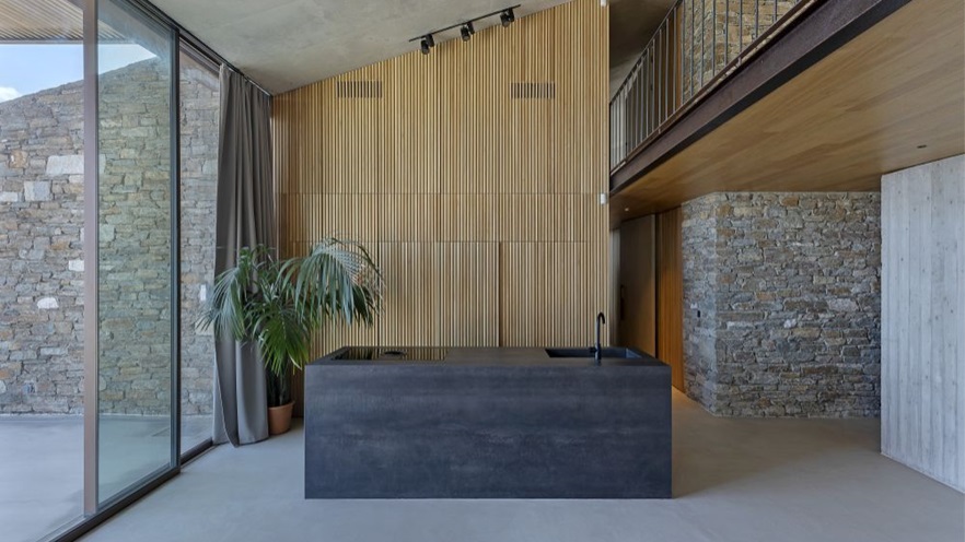 The kitchen counter is a concrete block in front of a wooden wall and a large window